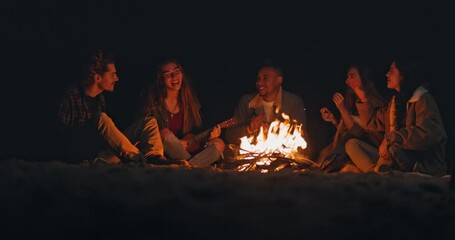 Group of friends singing playing ukulele at beach night bonfire - Powered by Adobe