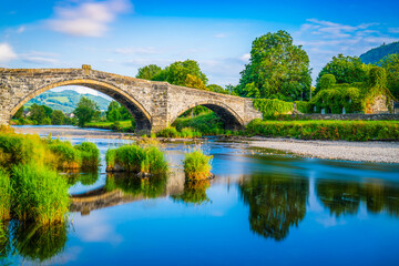 Fototapeta premium Stone bridge across the river Conwy and old cottage covered with vine leaves, Llanrwst, Caernarfon, North Wales