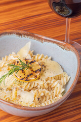 Fusilli pasta with parmesan and a glass of red wine on wooden table.
