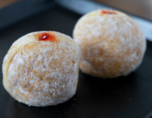 Strawberry jam filled donuts on a black plate, soft focus