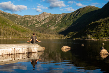 Back view of a young man meditating in front of the lake of the Americans, in the Gaspésie national park, Canada
