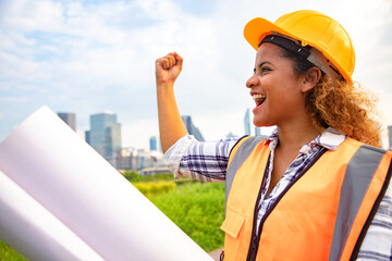 Portrait of woman architect standing with construction drawings roll paper in the public park. Back...