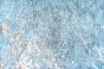 Sea ice texture. Frozen sea water with congealed small bubbles inside. The sea ice is pale blue. Embossed sea ice illuminated by the setting sun