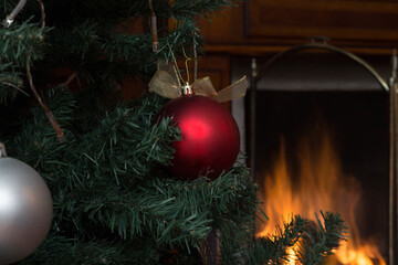 closeup of christmas tree with bulbs, in the background a fireplace is lit, celebration in the warmth of the home