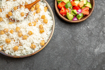 Homemade rice dish and salad with tomato and cucumber on dark table