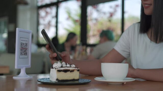 Women using their phones for scanning to pay for coffee and cake on cafe. Mobile scanning system online for pay money. Concept technology for pay by scan QR code.