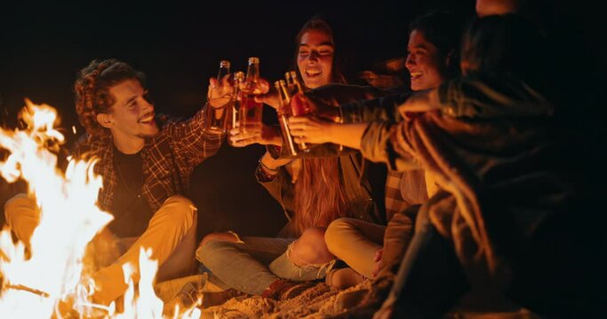 Group of friends toasting drinks on beach bonfire at night