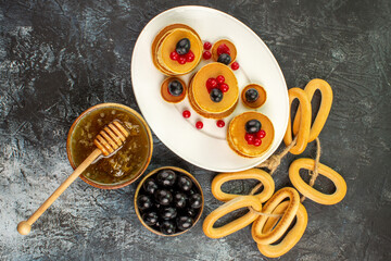 Above view of fruit pancakes cookies near honey in a bowl and black cherries on gray table