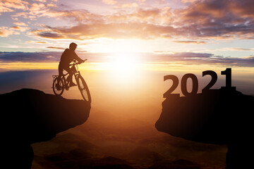 Success 2021 new year concept. Silhouette of cyclist riding between 2020 years with sunset...