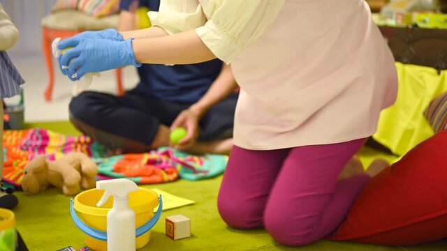 子供が遊ぶおもちゃを除菌スプレーで消毒する保育士