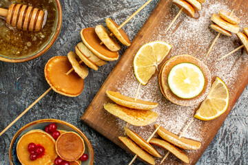 American pancakes with lemons on cutting board and honey with wooden spoon on gray table