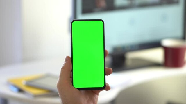 Over The Shoulder View Man at Home Sitting on a Chair Using with Green Mock-up Screen smartphone in Vertical Mode. Male Using Touchscreen Device, Browsing Internet, Watching Content