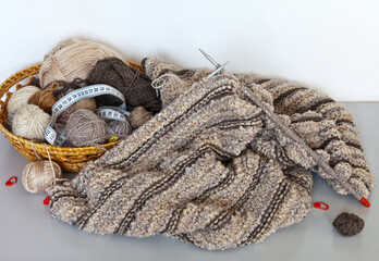 The process of knitting a warm striped sweater made of woolen and boucle yarn. Wicker basket with balls nearby. Hobby and needlework concept, winter leisure
