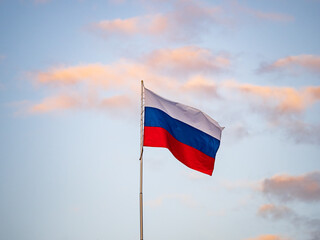Russian tricolor flag waving in the wind against a blue sky.