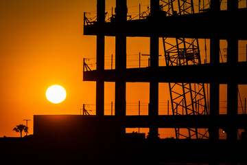 Iron and steel frame of commercial building including a crane at a construction site at sunset  at sunset with the sun visible
