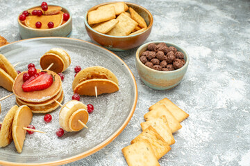 Side view of pancake decoration with fruits and biscuits on a white plate and white background
