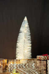 Small cone-shaped  white Christmas trees on a brown background decorated with a Christmas garland. Gift boxes.