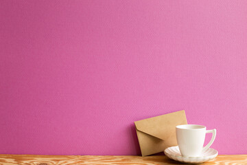 Coffee cup with kraft paper envelope on wooden table. pink background