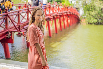 Obraz premium Caucasian woman traveler on background of Red Bridge in public park garden with trees and reflection in the middle of Hoan Kiem Lake in Downtown Hanoi. Vietnam reopens after coronavirus quarantine