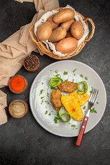 Vertical view of homemade cutlet meal along with potatoes with spices and towel on dark table