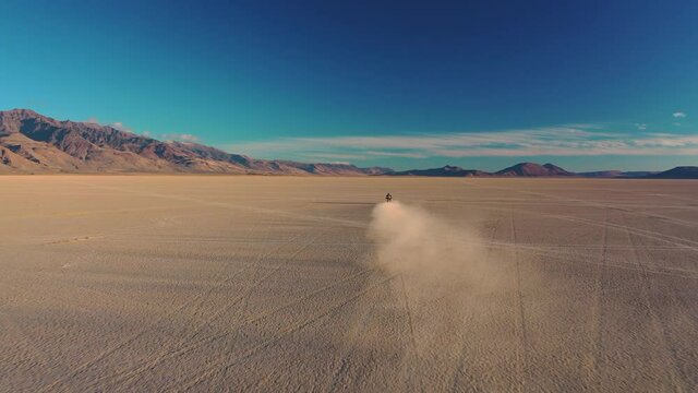 Yamaha Tenere T700 Adventure Motorcycle rider driving through desert sand dry salt lake with dust at sunset view with DJI Mavic 2 Pro Drone.