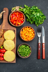 Tasty cutlets with vegetables with fork and knife on dark background
