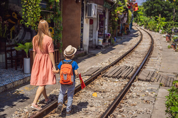 Mother and son travelers walk around railway paths which go through residential area in Hanoi city....