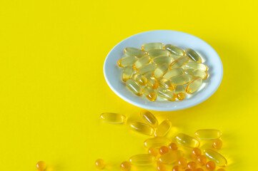 Fish oil capsules on yellow background, vitamin D, omega supplement, selective focus.