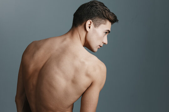 Sexy man with a naked back looks to the side on a gray background rear view of a fitness sport model