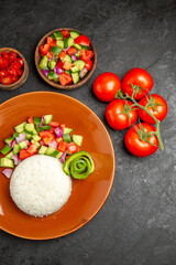 Vegan dinner with rice on a brown plate and different types of vegetables on dark table