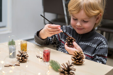 Christmas kids craft activities at home. Little child painting pine cones and wooden Christmas tree...