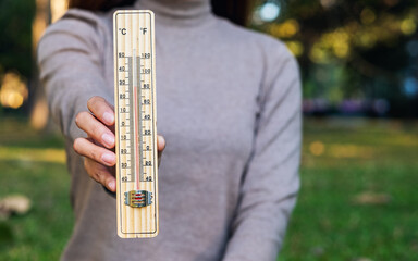 Closeup image of a woman holding and showing thermometer in the outdoors