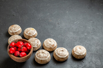 Horizontal view of tasty cookies and red cornel berries in a brown bowl on dark table