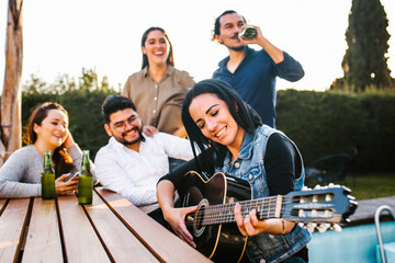 Latin friends drinking beer on the terrace and latin woman playin a guitar in Mexico city