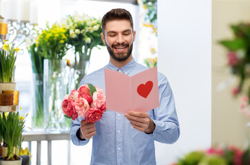 holidays, love and people concept - happy smiling man holding bunch of peonies and open valentine's day greeting card with heart over flower shop background