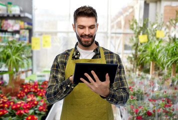 gardening, small business and sale concept - happy smiling male gardener or seller in apron and rubber boots with tablet pc computer over flower shop background