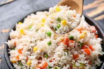 Bowl with tasty pilaf and wooden spoon on table