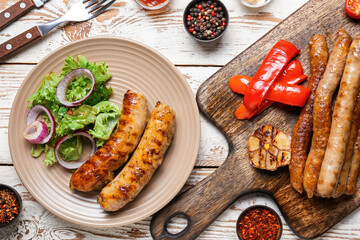 Plate with delicious grilled sausages, vegetables and spices on wooden table