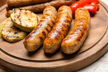Wooden board with delicious grilled sausages and vegetables on table, closeup