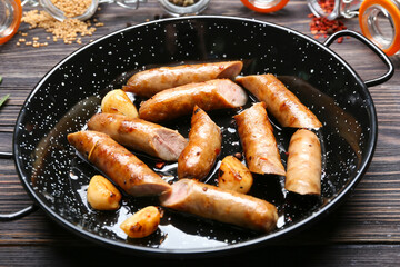 Frying pan with delicious grilled sausages on wooden table