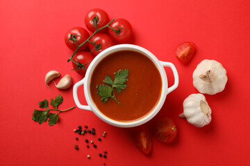 Bowl with tomato soup and ingredients on red background