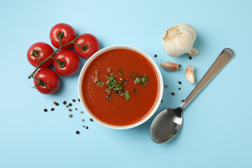 Bowl with tomato soup and ingredients on blue background