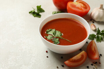 Bowl with tomato soup and ingredients on light background