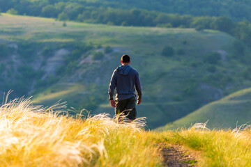 Naklejka na ściany i meble Man walking in a field on golden sunset