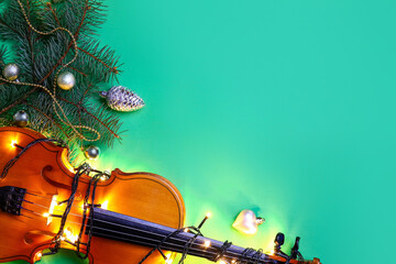 Violin with Christmas lights and decor on color background