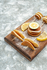 Vertical view of buttermilk pancakes with lemons on wooden cutting board on blue background