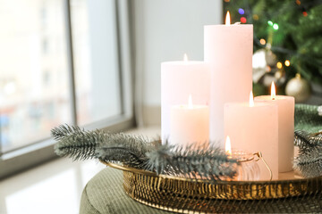 Tray with burning candles in room decorated for Christmas