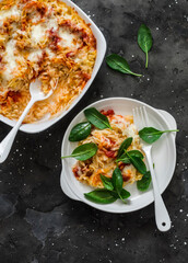 Roasted orzo pasta with tomato sauce and mozzarella cheese served with spinach on a dark background, top view