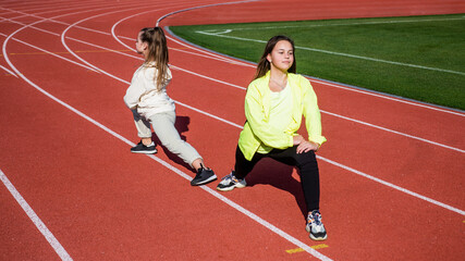 teenage girls stretching before run marathon. runners prepare for race competition. sprinter warming up on stadium gym. flexibility. children training at school physical education lesson