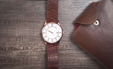 Brown wristwatch and wallet on the wooden background.